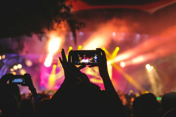 Eventfotografie Hände halten Smartphones, während auf einer Bühnenaufführung Lichter funkeln.